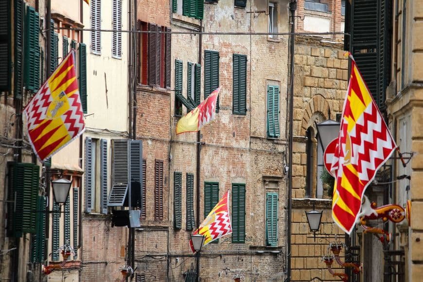 One Day in Siena, Colorful Contrade flags hanging in a Siena alley